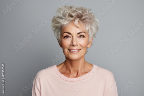 Beautiful senior woman with grey hair. Smiling mature woman looking at camera and standing against grey background