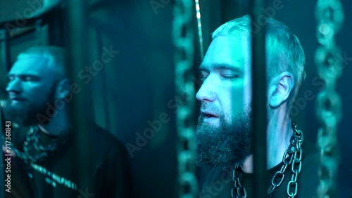 A young stylish man at the event standing with chains around his neck that hanging from the ceiling. Young drunk man in a night club in neon lights, concept of addiction to alcohol or drugs. photo