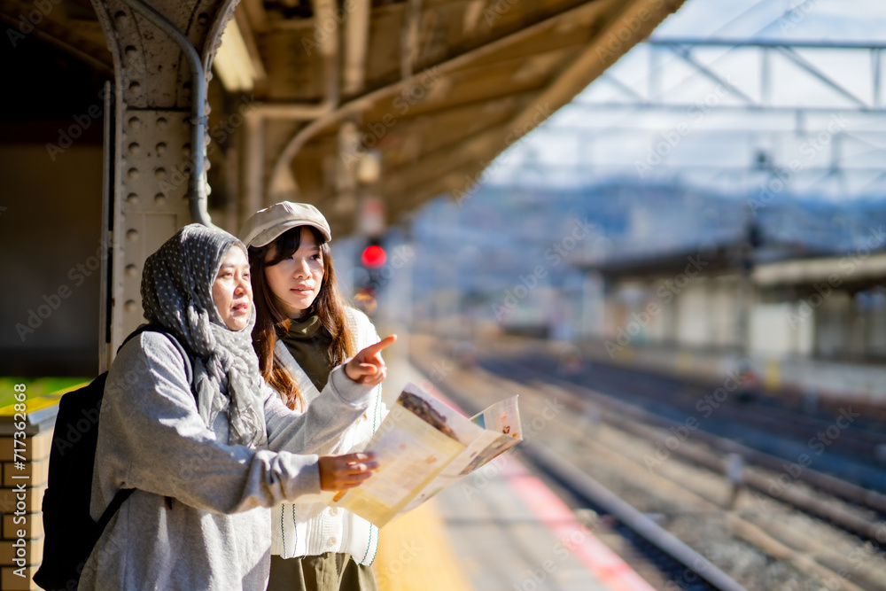 Fototapeta premium woman girl tourist Two Asian friends but different religions,They were looking at information about preparing to board the train at the train station,She is traveling in Japan. with fun, Japan travel 