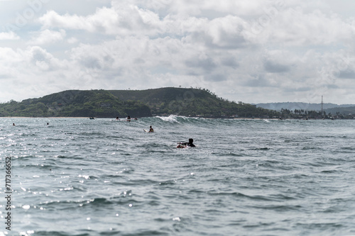 Local surfer paddling for riding waves on surfboard in reef break wave and backdrop of green hills, Indonesia, Asia photo