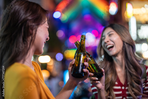 Asian woman friends hold bottle of beer, having party in front of bar. 