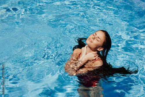 Happy woman swimming in the pool in red swimsuit with loose long hair in the sunshine  skin protection with sunscreen  concept of relaxing on vacation.