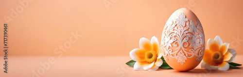 Easter egg with a carved white pattern and two delicate flowers to match the peach background