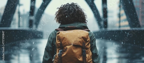 Student with curly hair and a backpack walks alone in bad weather and is interested in architecture, design, 3D, and rendering.