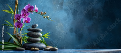 Blue background still life featuring bamboo plant, orchid, and stones.