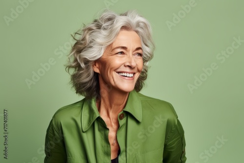 Smiling mature woman in green shirt looking at camera over green background © Inigo