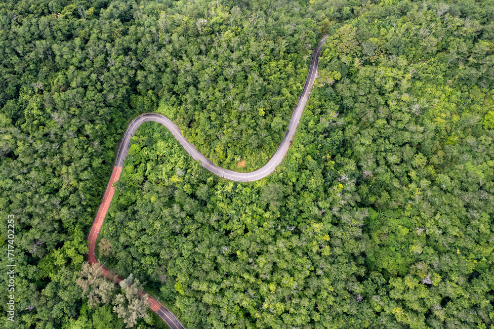 Top view of countryside road passing through the green forrest and mountain