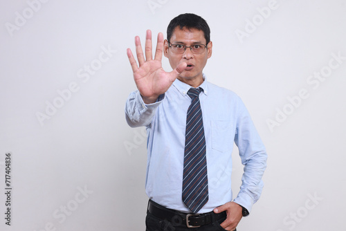 Adul Asian male wear glasses and formal shirt with tie showing stop gesture, saying no or not accepting a deal in an office at work