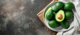 Top view of ripe avocados arranged on a white dish and wooden cutting board with cloth, creating a flat lay. Represents the concept of healthy fruits with space for text.