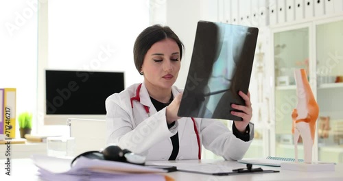 Traumatologist examines x-ray of leg and model of knee joint photo
