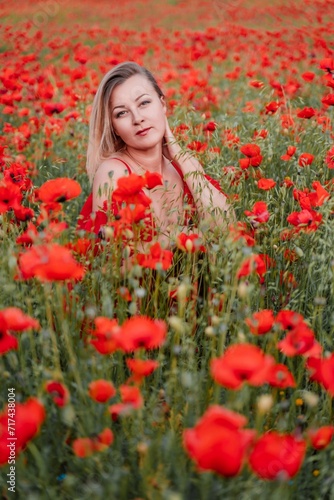 Happy woman in a red dress in a beautiful large poppy field. Blond sits in a red dress, posing on a large field of red poppies