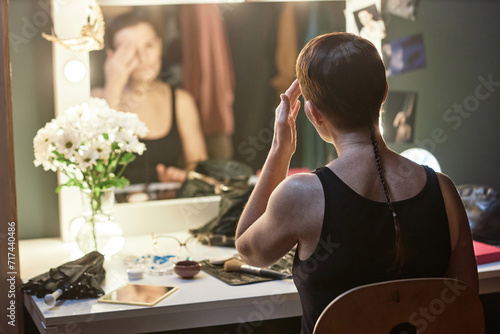 Back view of female artist doing make up by vanity mirror backstage in theater preparing for performance, copy space photo