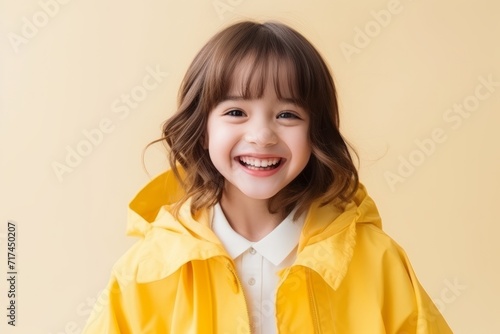 Portrait of happy smiling little girl in yellow raincoat over beige background
