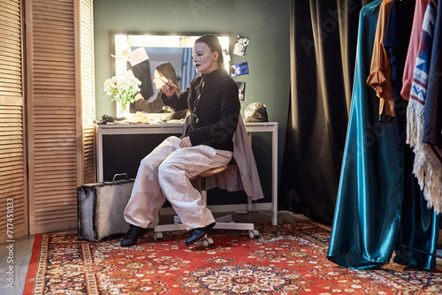 Full length portrait of female mime performer sitting by mirror backstage preparing for show in theater, copy space