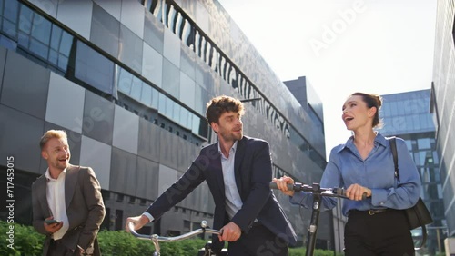 Joyful coworkers going street with eco scooter bicycle. Happy business people