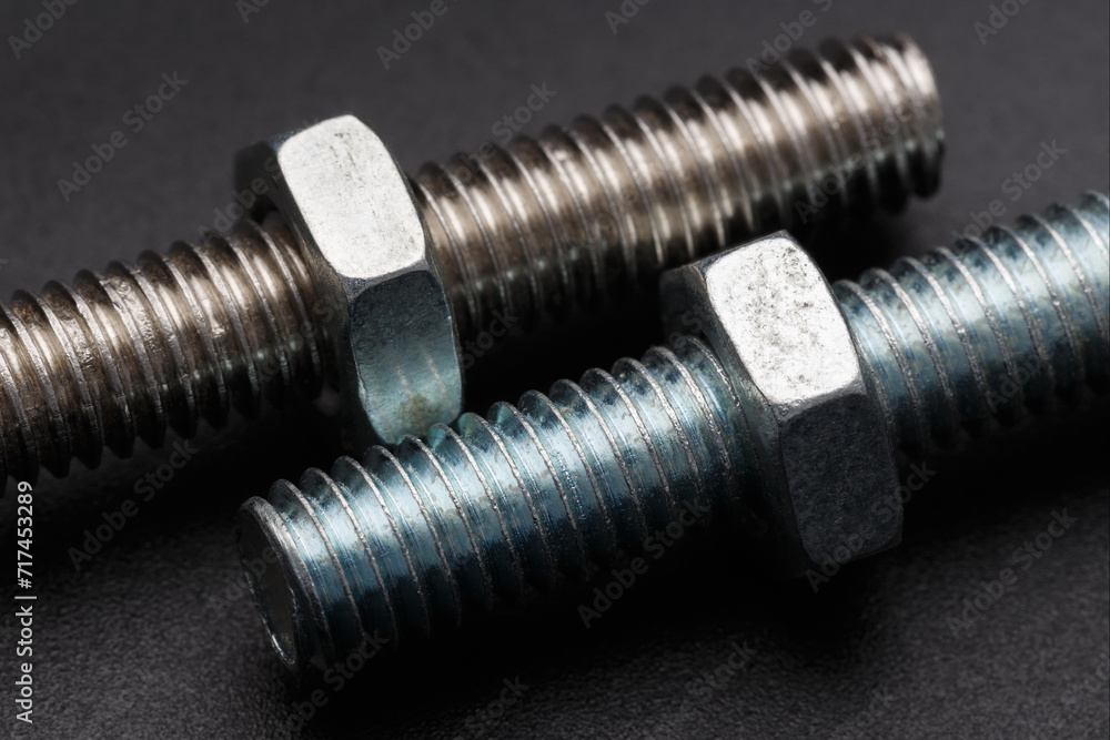 Two bolts with nuts on a dark background Two bolts with nuts on a dark background