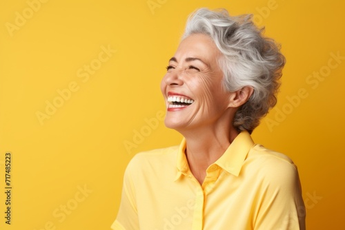 happy senior woman with grey hair laughing and looking up on yellow background