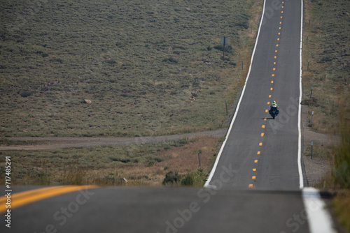 Billede på lærred A person traveling on a motorcycle on a long tarmac road on a hot Summer day