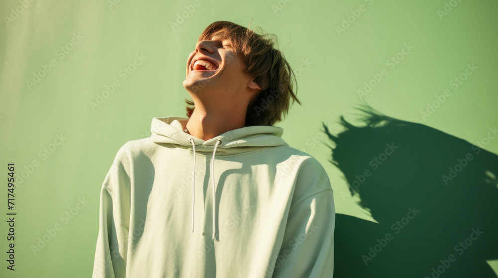 A teenage boy laughing heartily in a white hoodie, casting a playful shadow on a light green background.