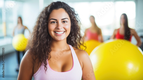 Radiant young woman holding a yellow fitness ball in a gym setting, representing a healthy lifestyle.