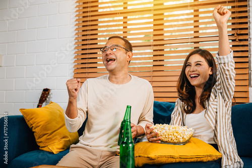 A jubilant Asian couple husband and wife cheer for a football goal during their leisure weekend creating an atmosphere of joy excitement and togetherness as dedicated sports enthusiasts. photo