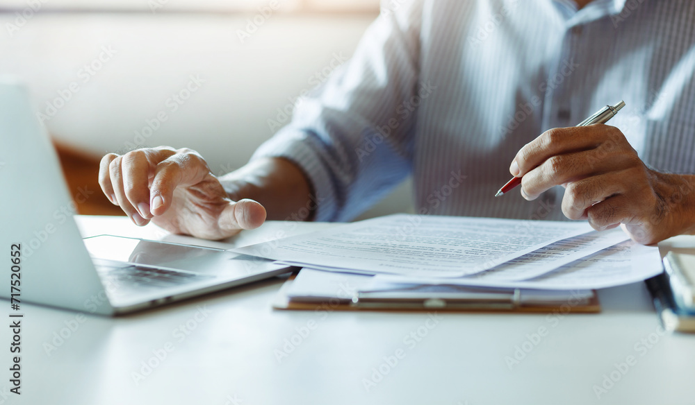 © Lek - Asian businessman using computer laptop working and reviewing document reports at office workplace. legal expert, professional lawyer reading and checking financial documents or insurance contract
