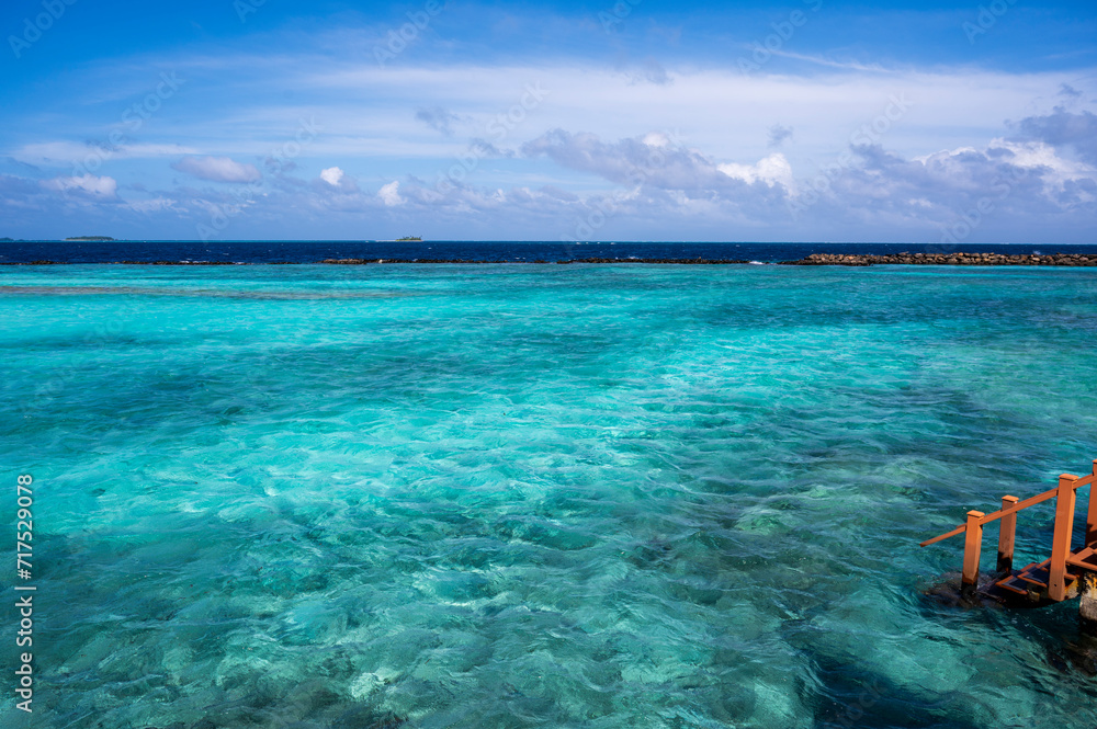 View of the pale blue water of the lagoon. In the background is a dark ocean. On the right, wooden steps into the water. View of the pale blue water of the lagoon. In the background is a dark ocean. On the right, wooden steps into the water.