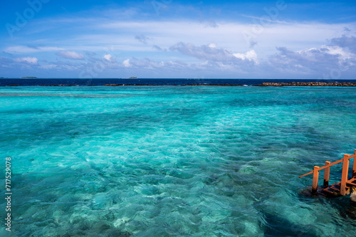 View of the pale blue water of the lagoon. In the background is a dark ocean. On the right, wooden steps into the water.