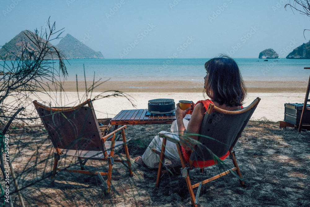 Women relaxing at camping tent near the sea at sunset.A young woman having breakfast drinking coffee in her caravan observing a good view of the beach.