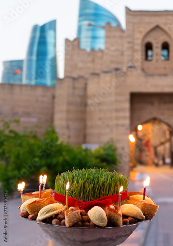 Novruz celebration festive tray or plate with green wheat grass and traditional national pastry - pakhlava, shekerbura and candles with Baku old city in the background 