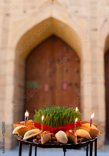 Novruz celebration festive tray or plate with green wheat grass and traditional national pastry - pakhlava, shekerbura and candles with Baku old city in the background 