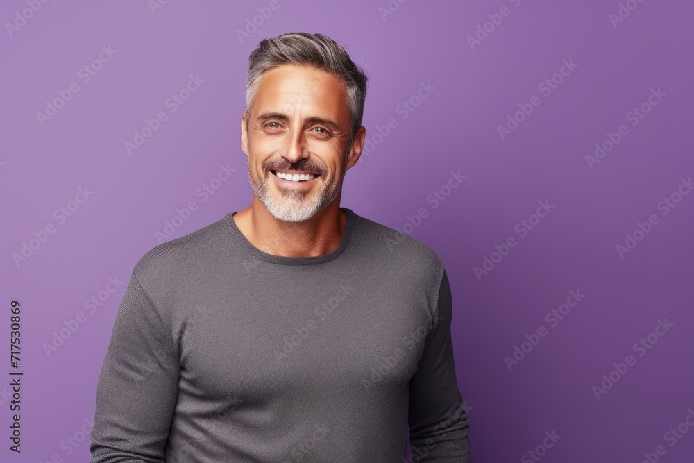 Handsome mature man looking at camera and smiling while standing against purple background Handsome mature man looking at camera and smiling while standing against purple background