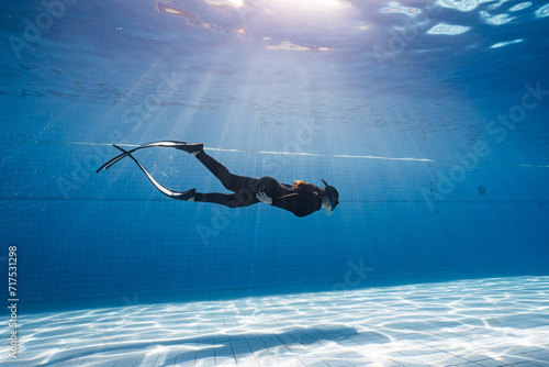 Beauty freediver Asian women diver with fins glides underwater in transparent blue pool. Freediver glides over swimming pool with black fins. Attractive woman free diver in blue pool.