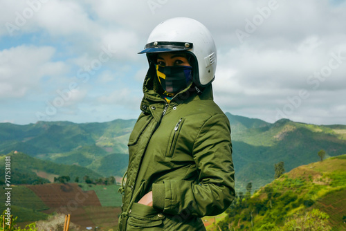 Female motorcyclist standing with her enduro motorcycle on mountain top, peaks skyline view and Wear a helmet. Motorcycle rider enjoying the view.