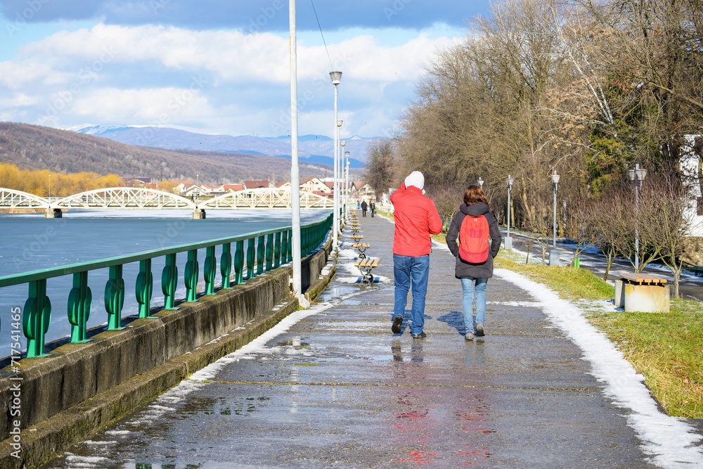 Two young people - a boy and a girl - were walking on the wet path of the lakeside park on a winter's day.
