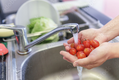 Woman hands washing fresh red cherry tomatoes in kitchen