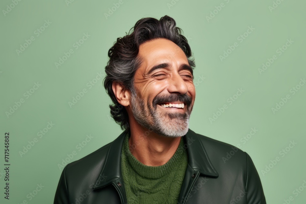 Portrait of handsome middle-aged man with gray hair and beard wearing black leather jacket and green knitted sweater. Isolated on green background Portrait of handsome middle-aged man with gray hair and beard wearing black leather jacket and green knitted sweater. Isolated on green background