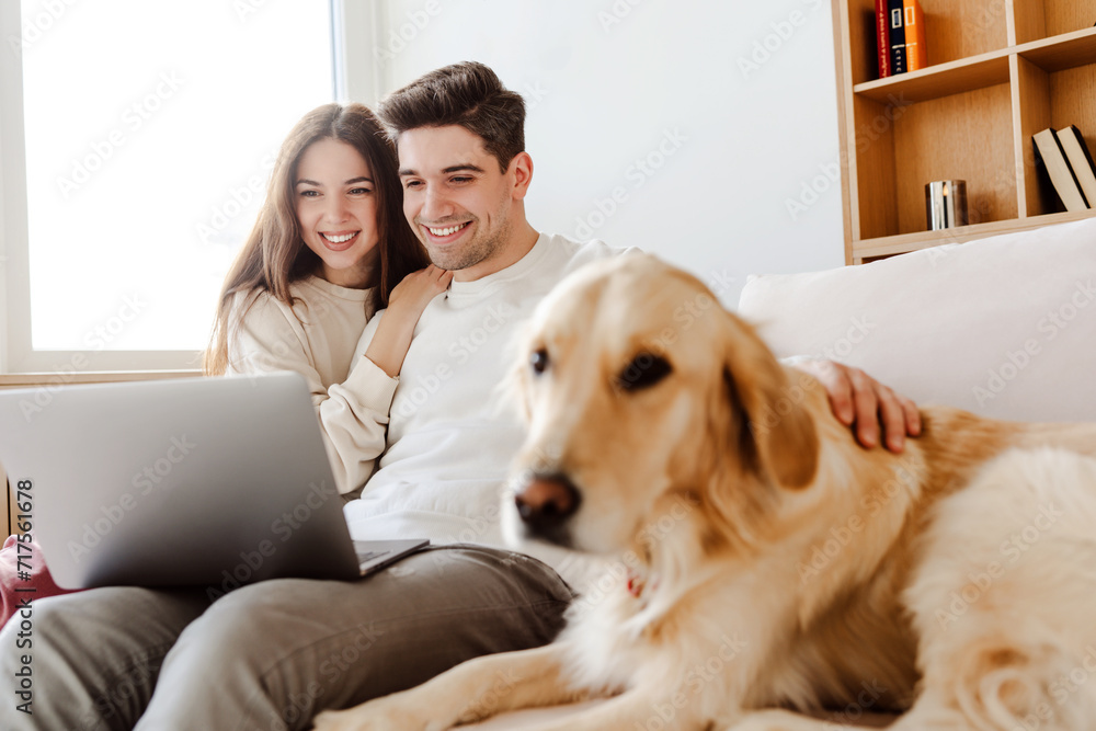 Portrait smiling couple hugging, dog, golden retriever, selective focus using laptop online shopping Portrait smiling couple hugging, dog, golden retriever, selective focus using laptop online shopping