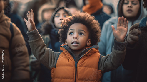 A black child with hands raised with a background of people demonstrating