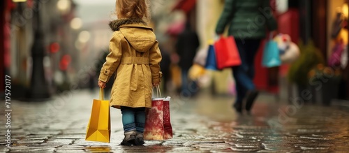 full length of cheerful kid in trench coat and jeans standing near shopping bags with soft toy on grey. Copy space image. Place for adding text or design