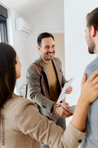 A young, beautiful, and excited married couple expecting a baby, just decided to buy a property from a real estate agent who is giving tem a key of their new home