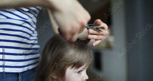 Woman doing haircut to child in an apartment. Mom cuts babys hair with scissors. Hairstyle for child at home. Buy scissors for beginning hairdresser. Hairdresser works with clients at home