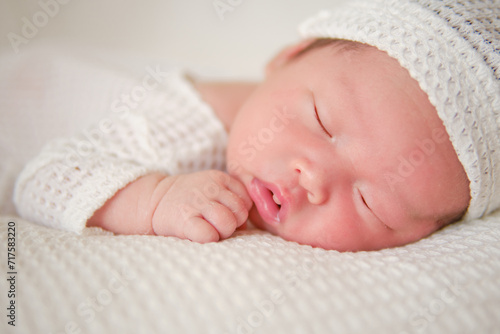 Close up of sweet face of a newborn boy. The asian baby boy wearing white suit and lying in a white blanket
