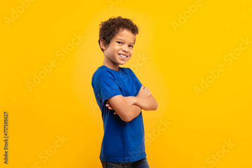 Confident boy with arms crossed in blue shirt on yellow background photo