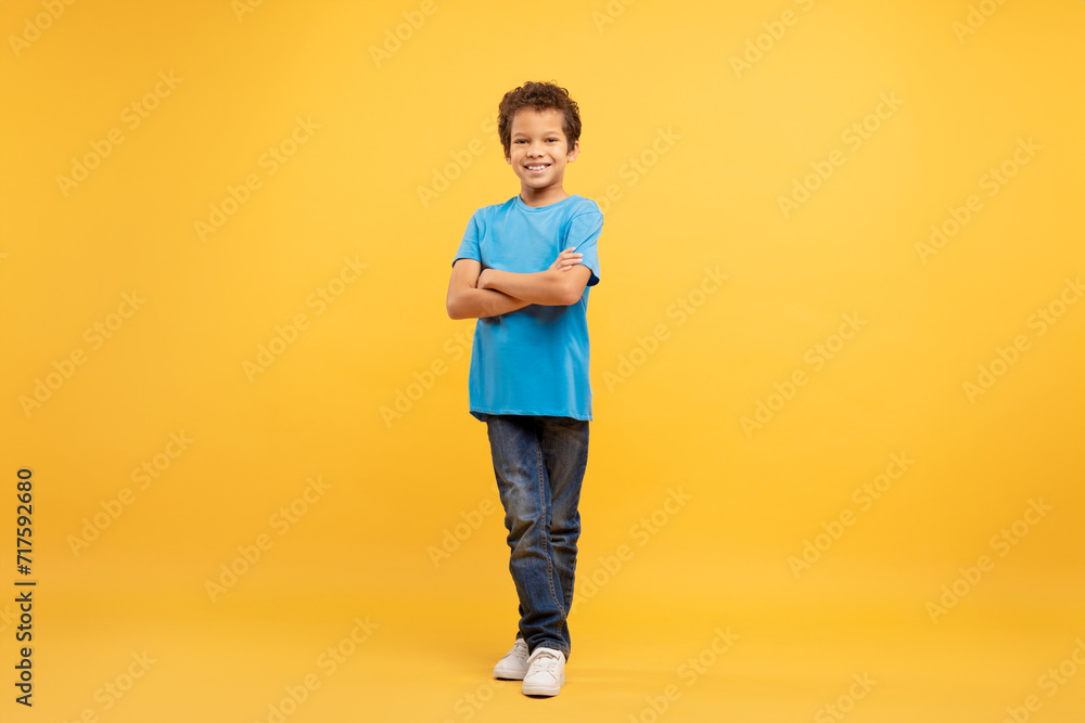 Confident latin boy with arms crossed in blue shirt, yellow background Confident latin boy with arms crossed in blue shirt, yellow background