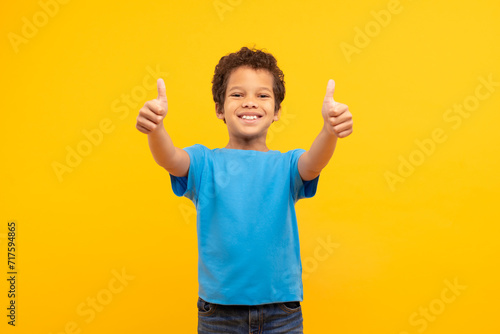 Cheerful boy with thumbs up in blue, vibrant yellow background