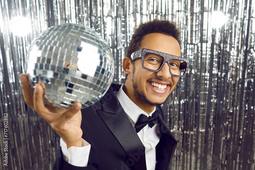 Portrait of overjoyed black man in suit and glitter glasses hold disco ball celebrate in nightclub. Smiling African American male entertainer or mc entertain public at party. Entertainment concept.