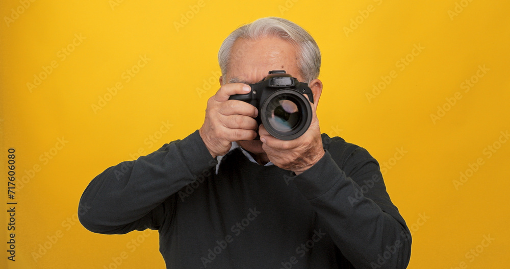 Old Asian man taking photo with digital camera, isolated on yellow background in the studio. Old Asian man taking photo with digital camera, isolated on yellow background in the studio.
