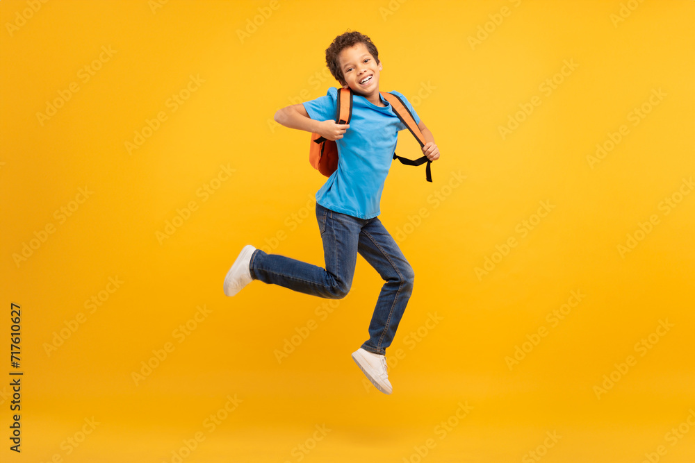 Energetic boy with backpack jumping, bright yellow background