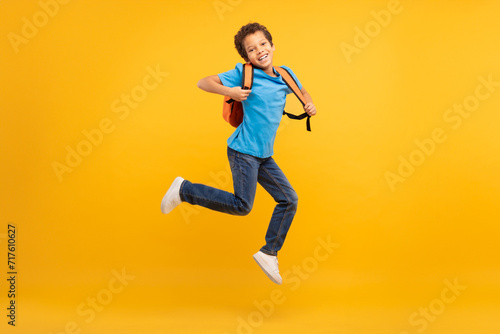 Fototapeta Naklejka Na Ścianę i Meble -  Energetic boy with backpack jumping, bright yellow background